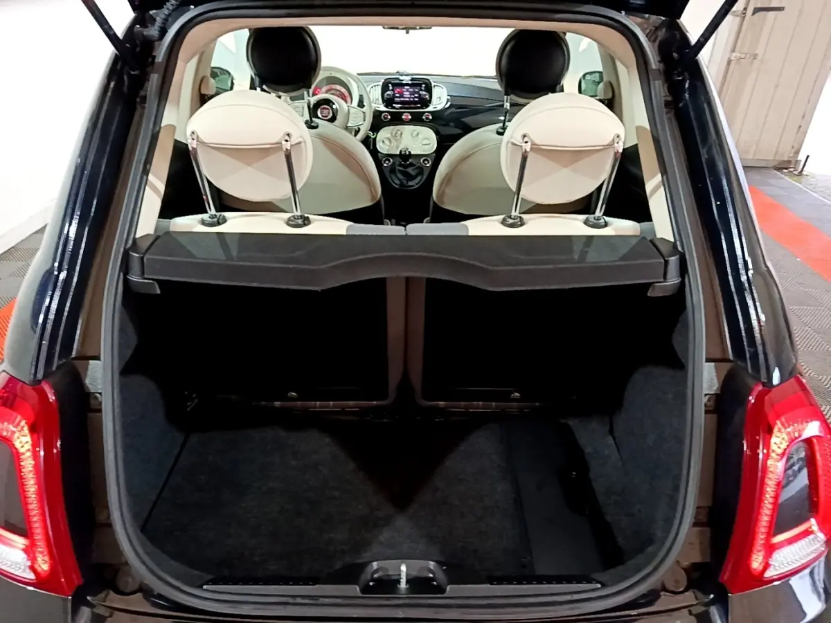 Coffre ouvert d’une Fiat 500 noire vue arrière, intérieur beige avec tableau de bord et écran tactile visibles.