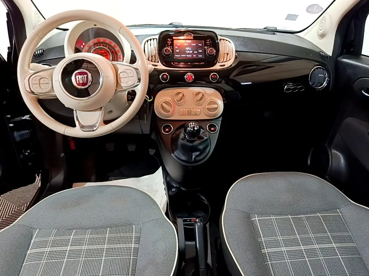 Vue intérieure avant de la Fiat 500 Lounge 2019, volant beige, tableau de bord noir brillant avec écran tactile central.