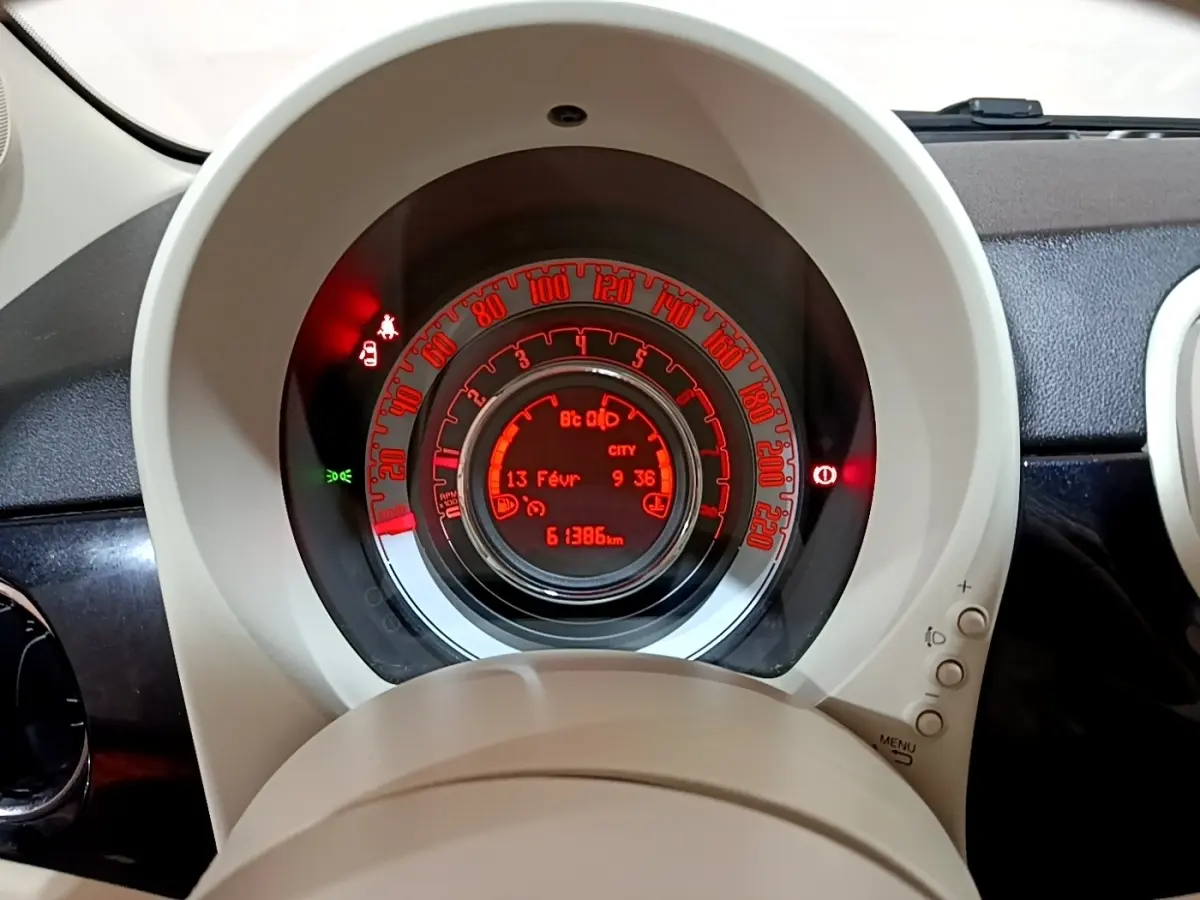 Vue rapprochée du tableau de bord central rougeoyant de la FIAT 500 Lounge 2019 avec affichage digital et compteur circulaire.