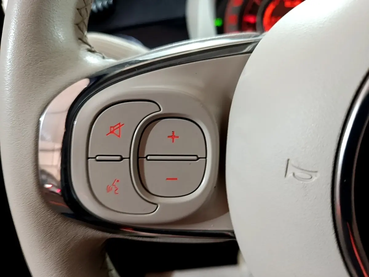Gros plan sur les commandes du volant cuir beige de la Fiat 500 Lounge noire, avec boutons de volume et commande vocale.