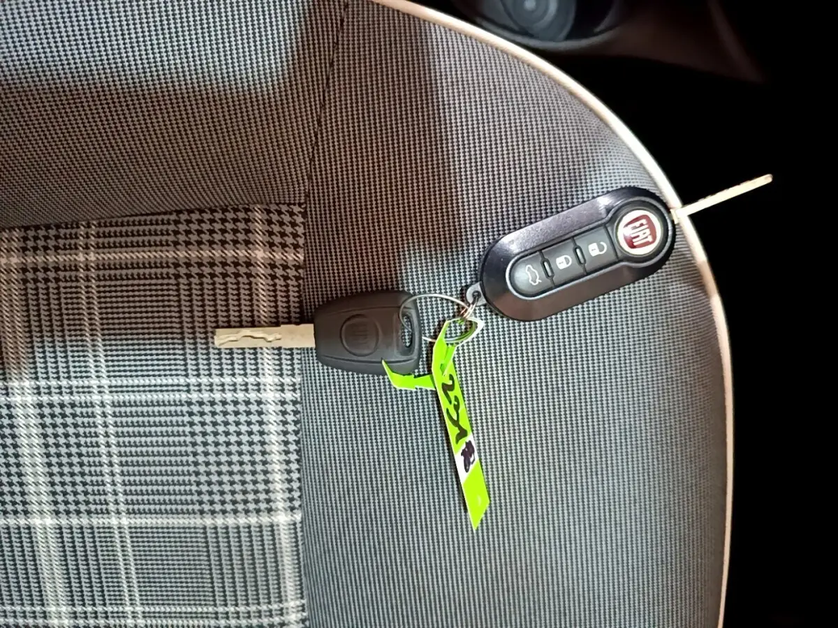 Clé et télécommande FIAT posées sur un siège tissu gris à motifs carreaux, intérieur d'une FIAT 500 noire.