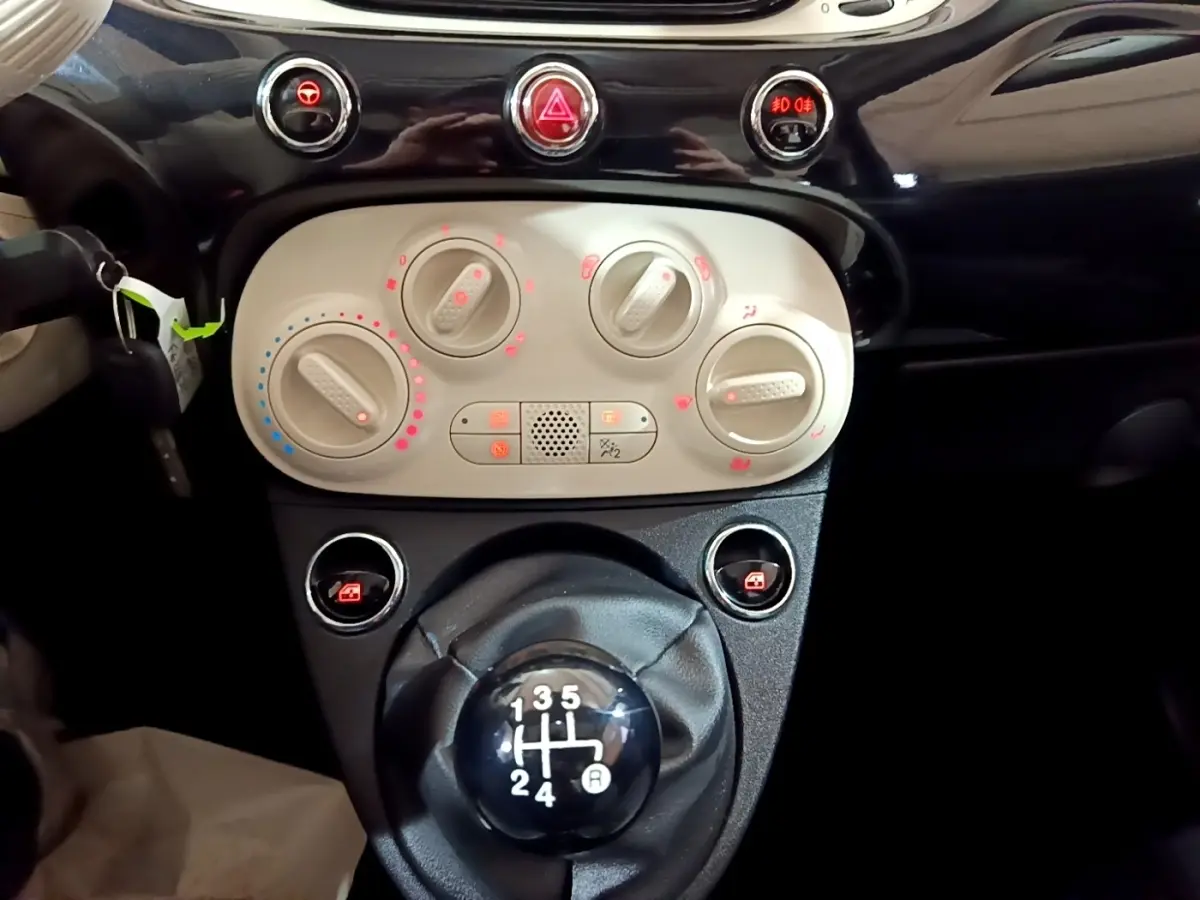 Gros plan sur la console centrale et levier de vitesses manuelle de la Fiat 500 noire, avec commandes de climatisation visibles.