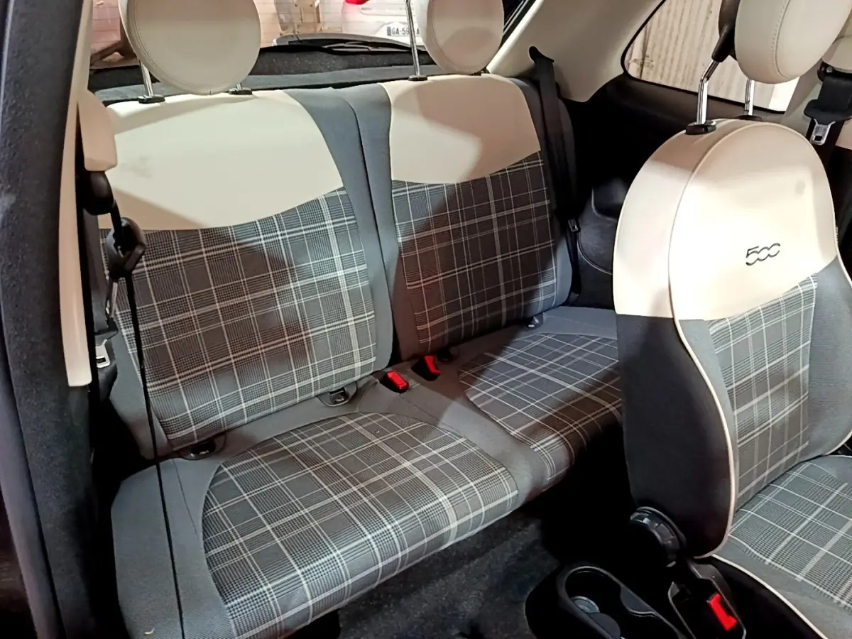 Vue intérieure sur les sièges arrière et avant d’une FIAT 500 noire, avec sellerie à motif écossais gris et beige.