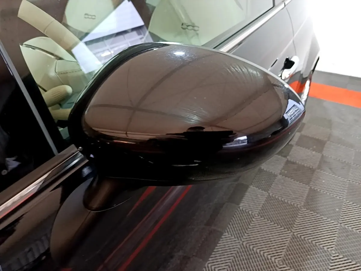 Rétroviseur côté gauche noir brillant d'une Fiat 500 Lounge 2019, avec intérieur beige visible en arrière-plan.