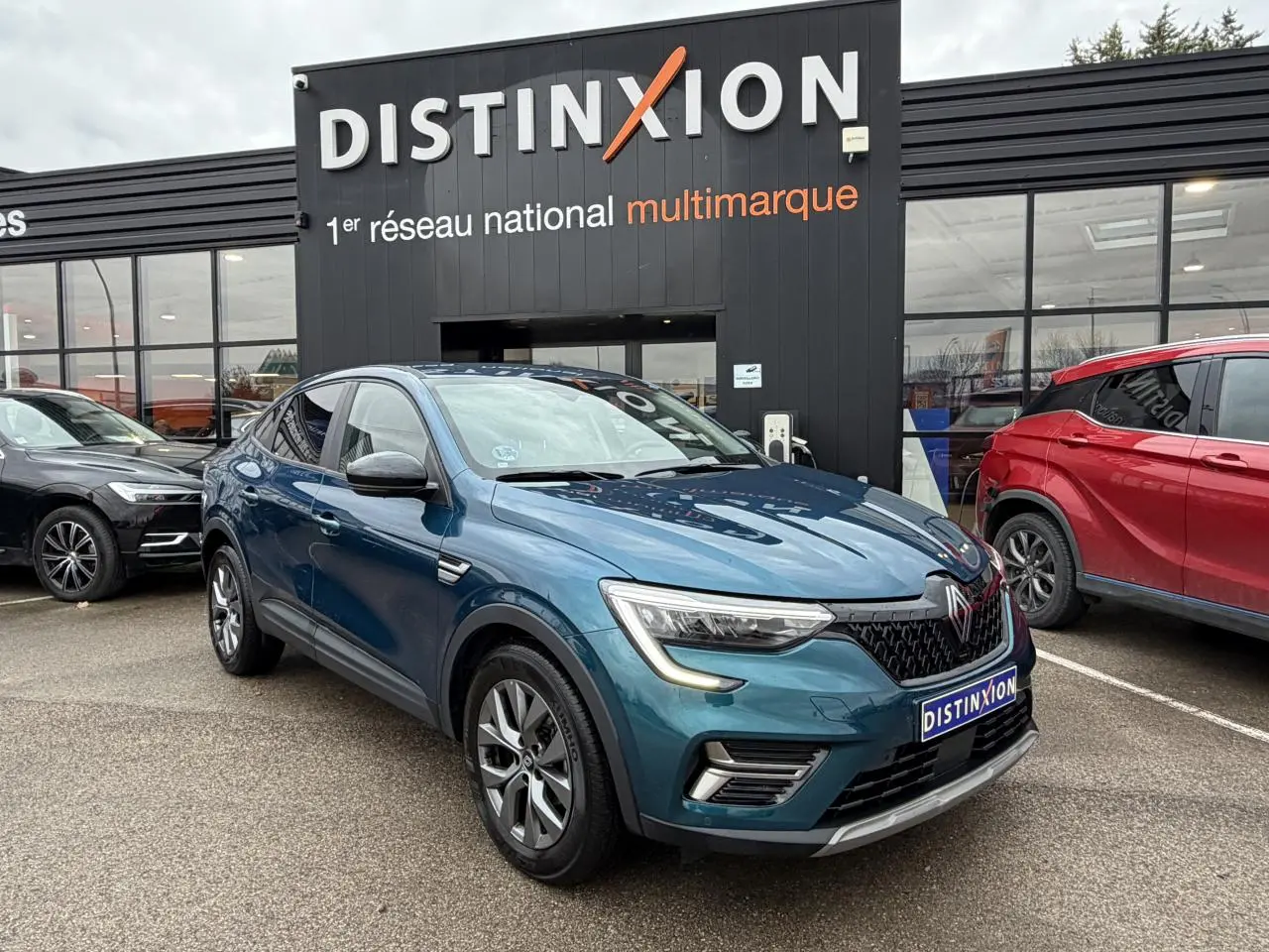 Renault Arkana bleu Zanzibar en 3/4 avant droit, avec jantes alliage et calandre noire distinctive, devant un showroom.