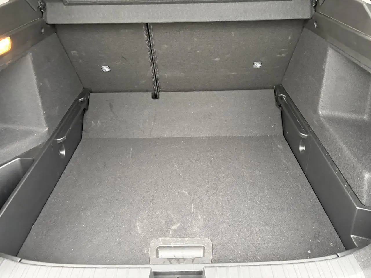 Vue plongeante sur le coffre spacieux et plat du Renault Arkana 2025, revêtement noir et rangements latéraux intégrés.