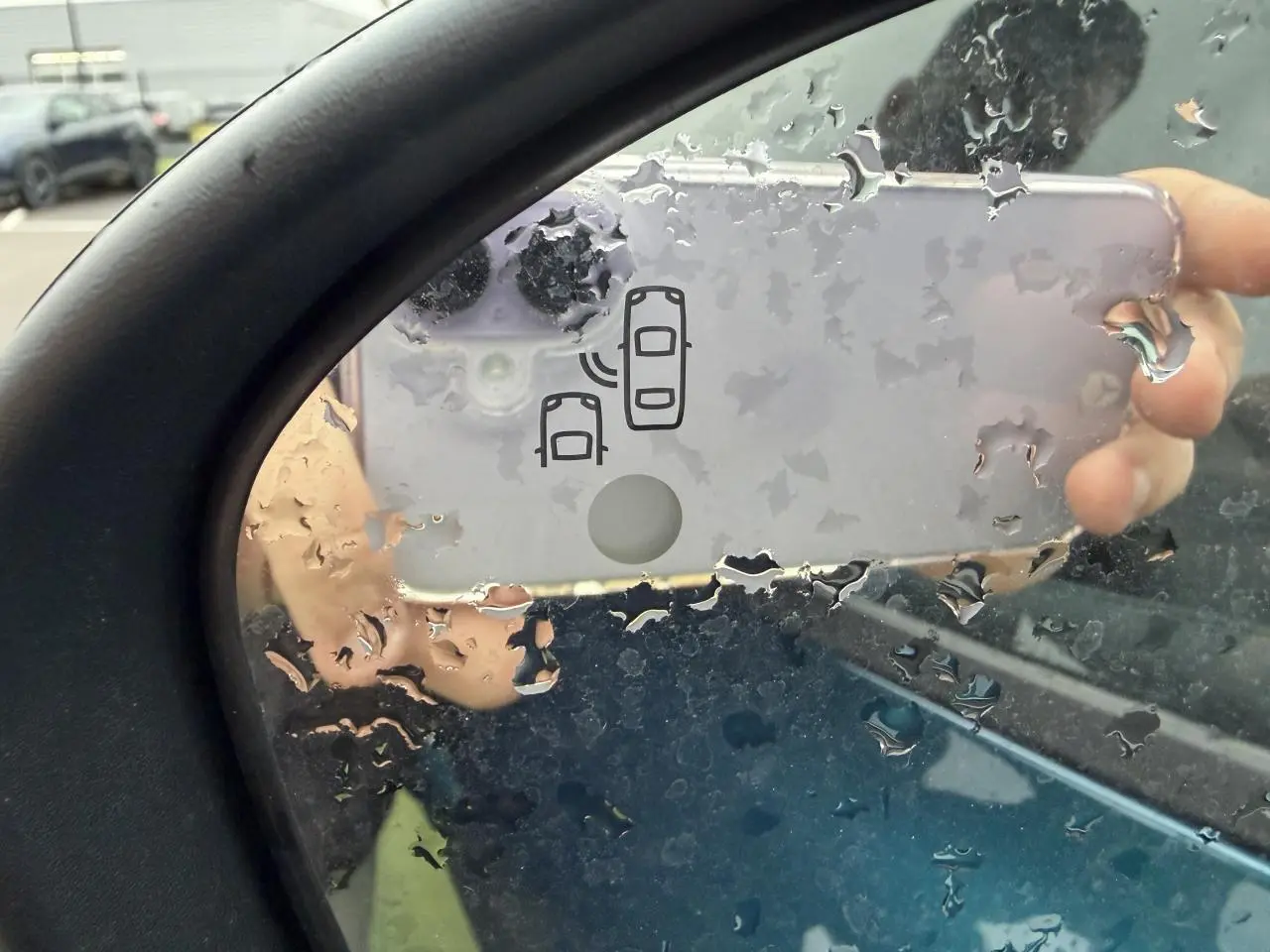 Rétroviseur côté gauche d'un Renault Arkana bleu Zanzibar, avec icône d'alerte d'angle mort visible sous la pluie.