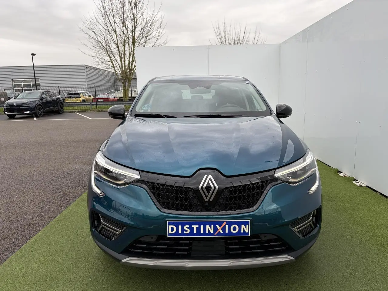 Vue frontale d'un Renault Arkana bleu Zanzibar métallisé avec calandre noire et phares LED allumés.