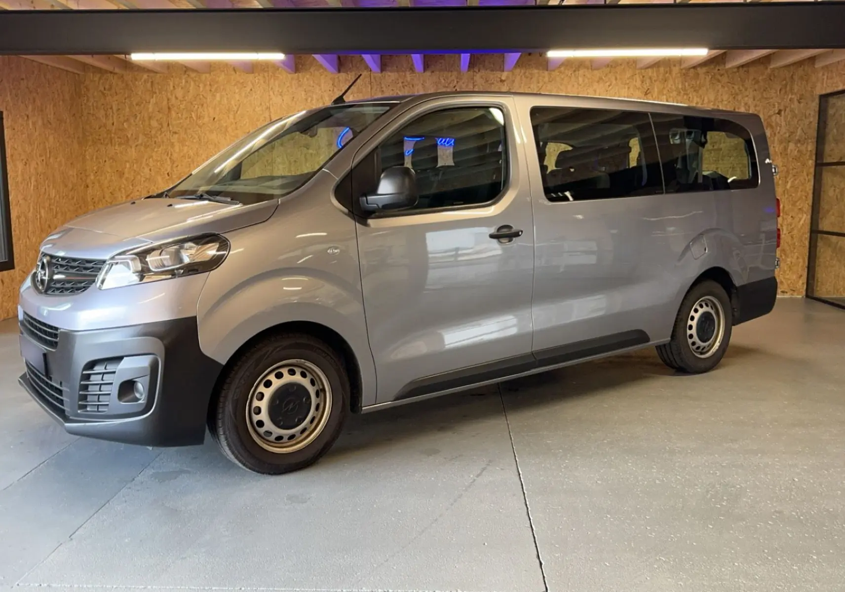 Vue 3/4 avant droit d'un Opel Vivaro Combi gris 2022 avec jantes acier et pare-chocs noirs dans un garage.