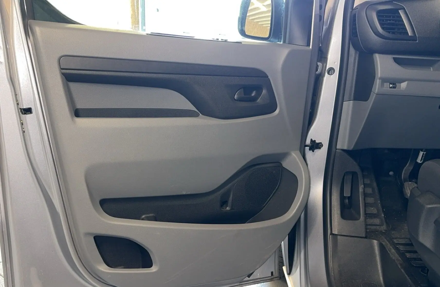 Intérieur côté gauche de la porte avant grise d'un Opel Vivaro Combi 2022, avec panneau de porte en plastique gris et noir.