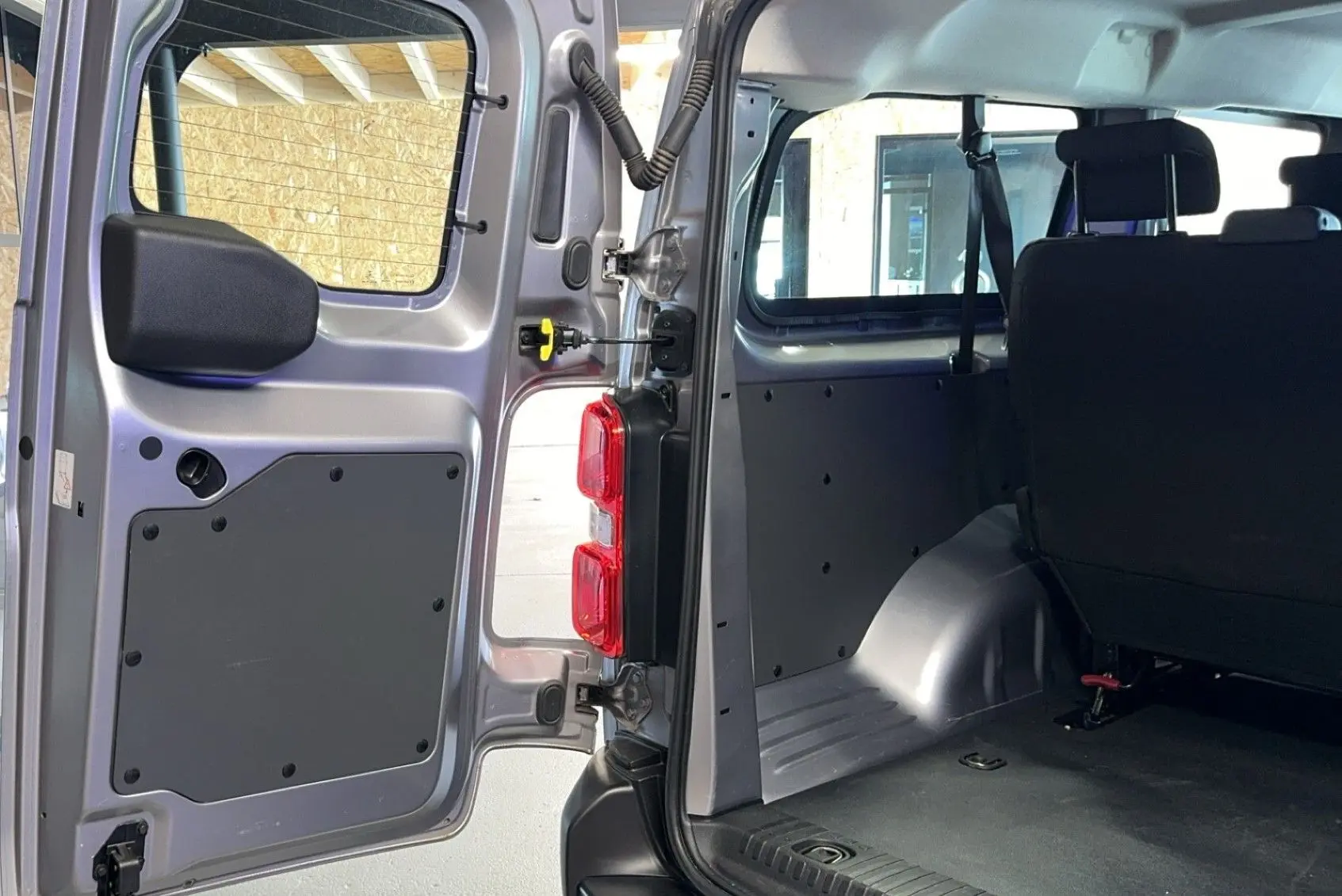Vue intérieure arrière gauche d'un Opel Vivaro Combi gris 2022, montrant la porte ouverte et les sièges en tissu noir.