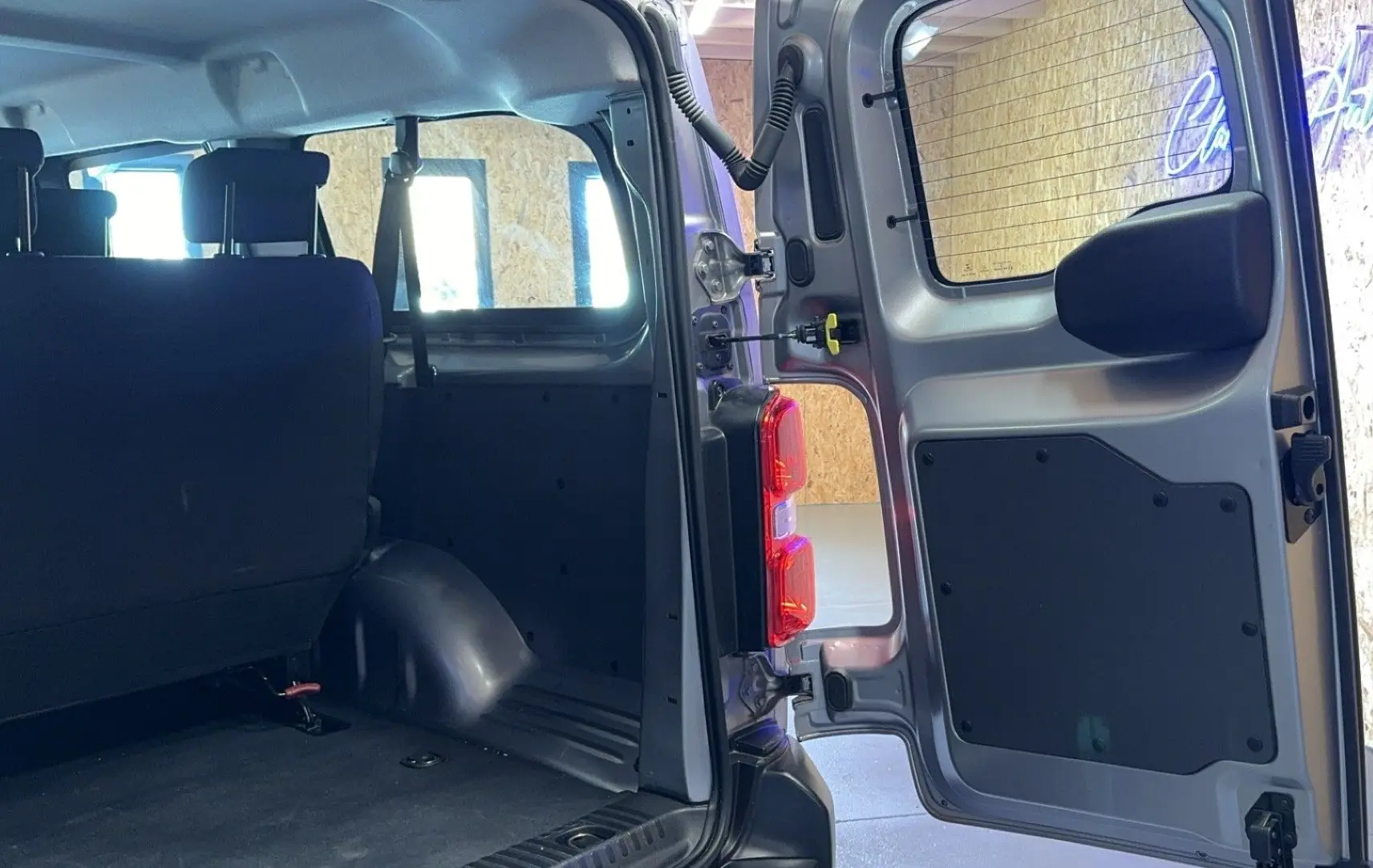 Vue intérieure arrière du gris Opel Vivaro Combi 1.5 Diesel 120 avec porte arrière ouverte et sièges en tissu noir.