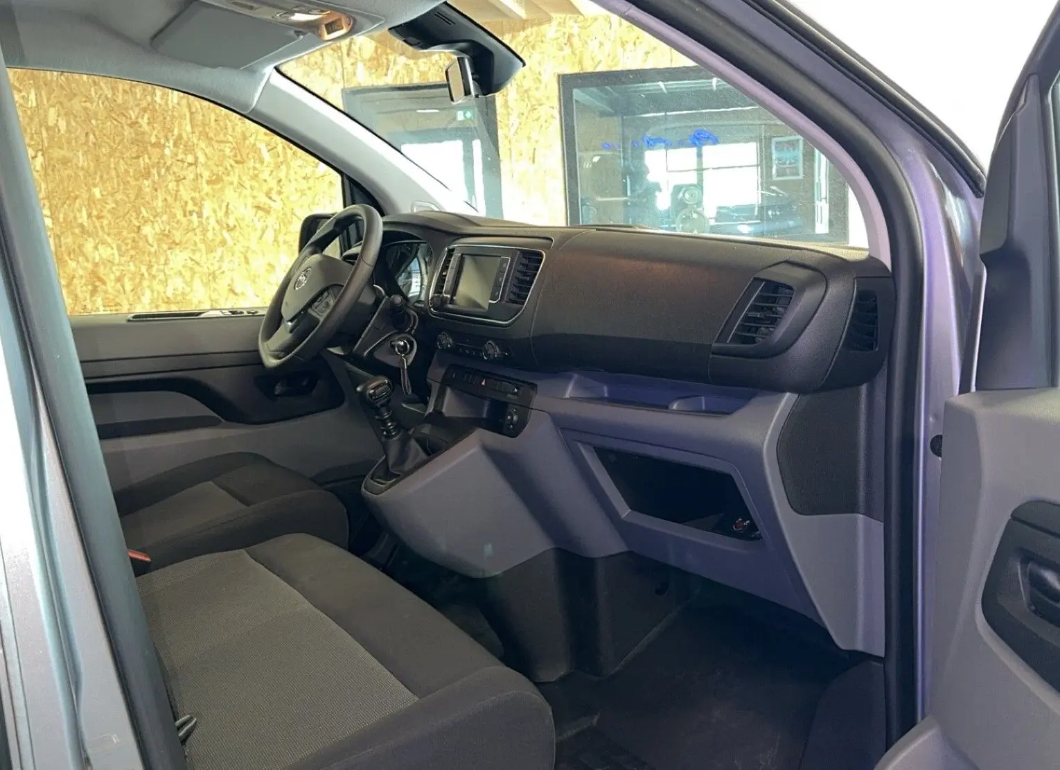 Intérieur avant droit de l'Opel Vivaro Combi gris 2022, avec tableau de bord et sièges en tissu noir.
