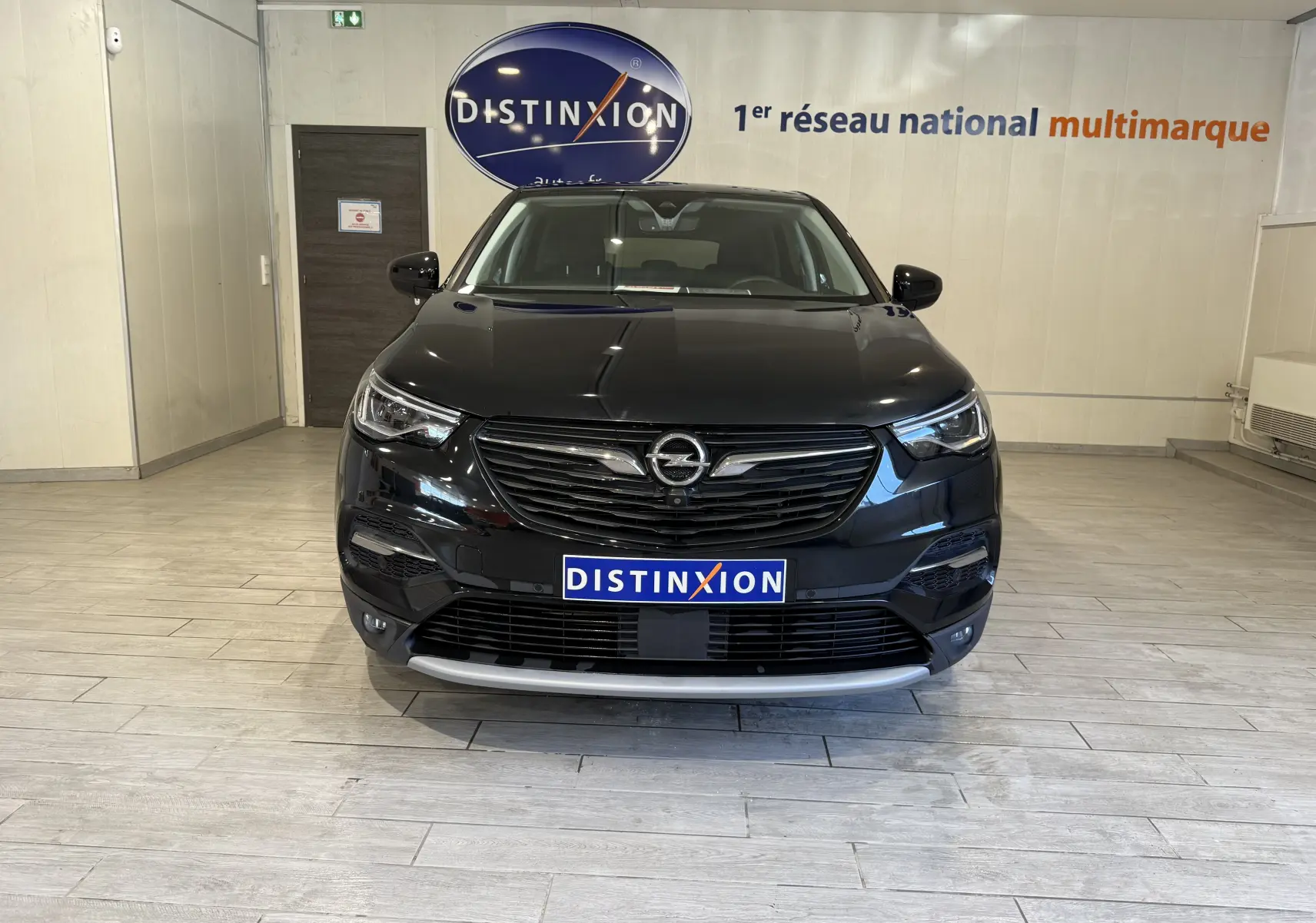 Vue frontale d'un Opel Grandland X noir métal, hybride rechargeable, avec calandre et logo Opel bien visibles en intérieur showroom.