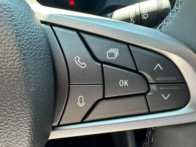 Gros plan sur les commandes multifonctions au volant côté droit du Dacia Duster blanc 2025, boutons appel et navigation.