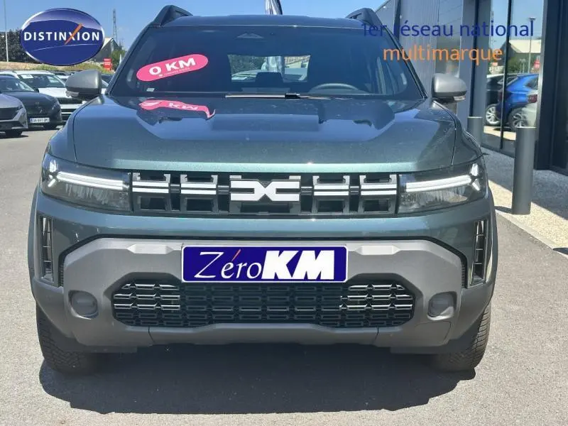 Vue frontale d'un Dacia Duster 2025 gris avec calandre noire et phares LED étirés, en extérieur sur parking.