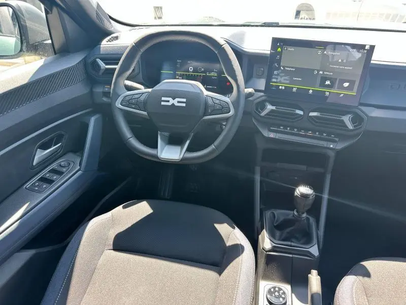 Vue intérieure du tableau de bord du Dacia Duster 2025 avec volant multifonction, écran tactile et levier de vitesses manuel.