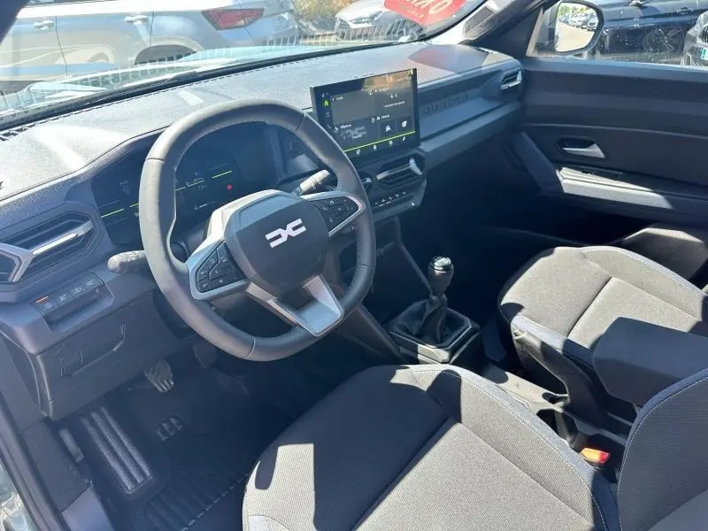 Vue intérieure côté conducteur du Dacia Duster 2025 avec volant multifonction, écran tactile et boîte manuelle noire.