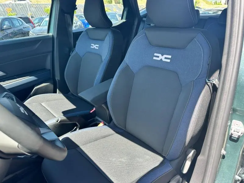 Vue intérieure sur les sièges avant bleu denim et noir du Dacia Duster 2025, avec logo Dacia brodé sur les appuie-têtes.