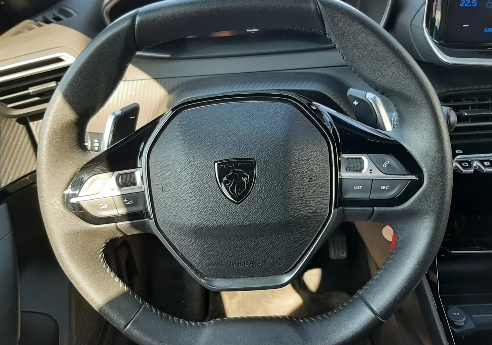 Vue rapprochée du volant cuir noir du Peugeot 2008 Hybrid 145 Allure 2025 avec commandes intégrées et tableau de bord partiel.