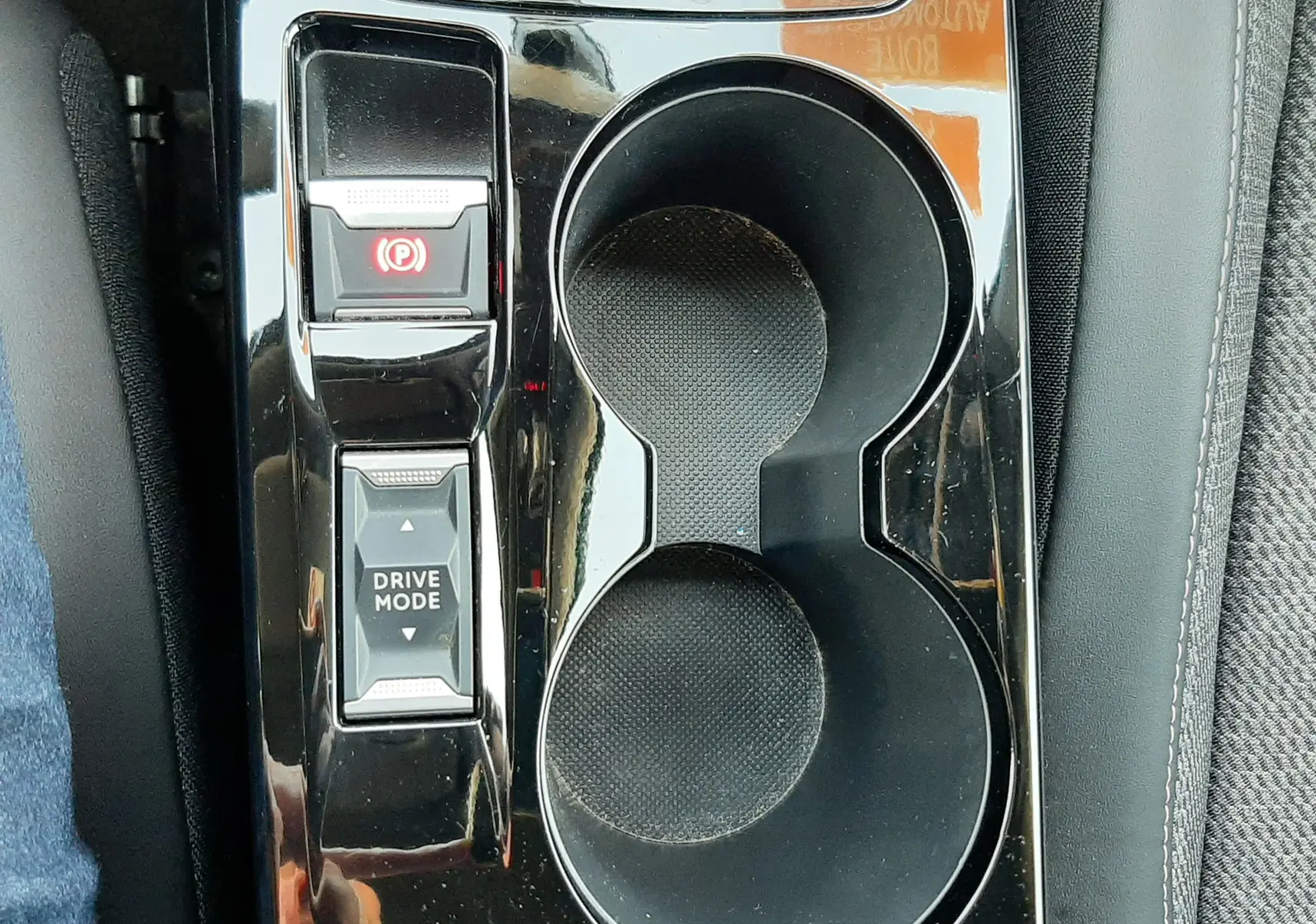 Gros plan sur la console centrale noire brillante du Peugeot 2008 Hybrid 145 Allure avec boutons frein à main et mode de conduite.