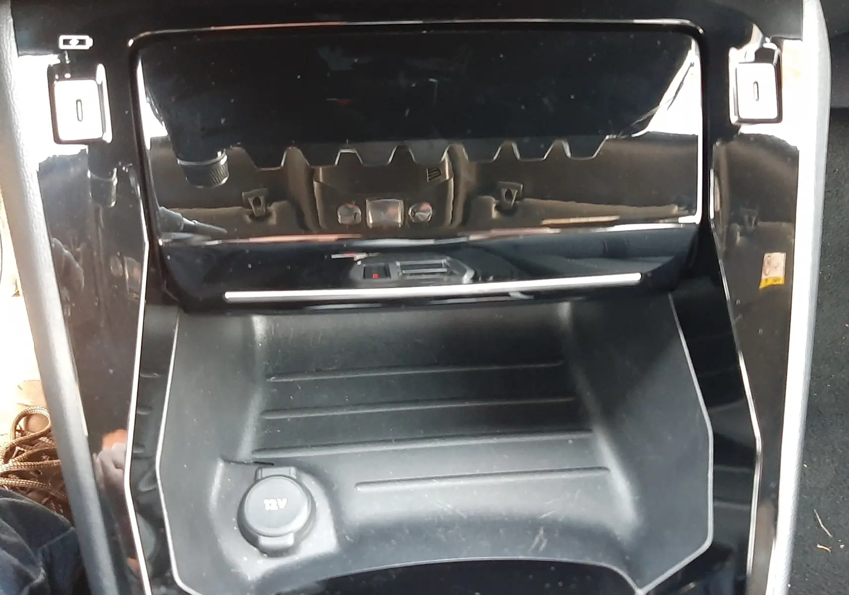 Gros plan sur la console centrale noire brillante du Peugeot 2008 Hybrid 145 Allure, avec prise 12V visible.