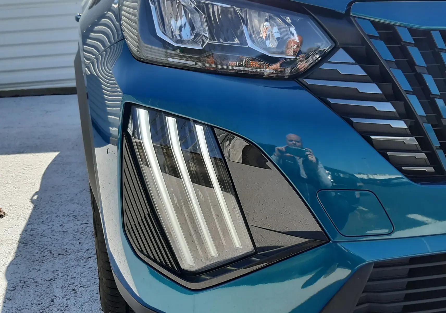 Gros plan sur le phare avant gauche bleu obsession du Peugeot 2008 Hybrid 145 Allure 2025 avec signature lumineuse verticale.