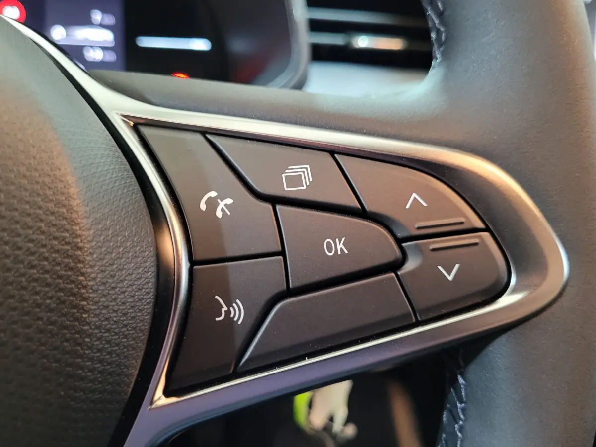 Gros plan sur les commandes multifonctions noires du volant côté gauche de la Renault Clio gris foncé 2025.