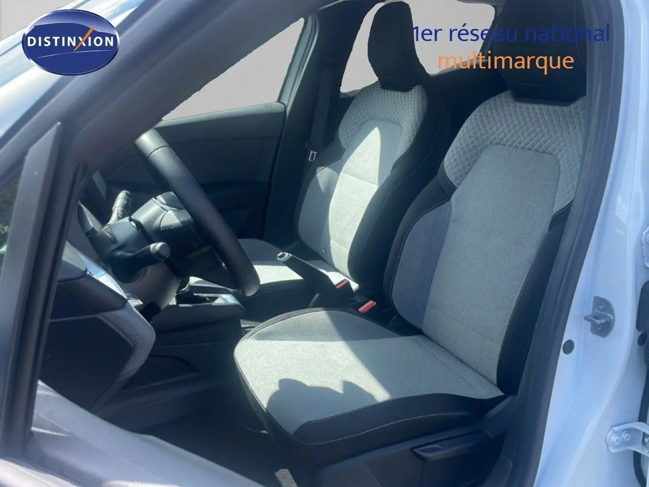 Vue intérieure côté conducteur de la Renault Clio blanche 2025, mettant en valeur les sièges tissu gris et noir et le volant multifonction.