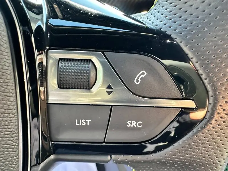 Gros plan sur les commandes noires du volant cuir perforé du Peugeot 2008 Gris Artense, boutons LIST, SRC et téléphone.