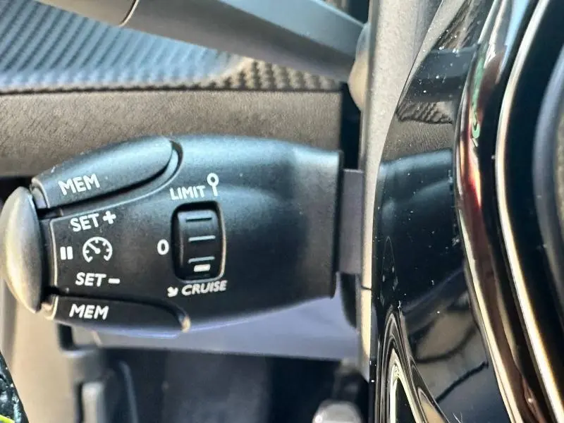 Gros plan sur la commande de régulateur de vitesse noire à gauche du volant d'une Peugeot 2008 gris Artense 2022.
