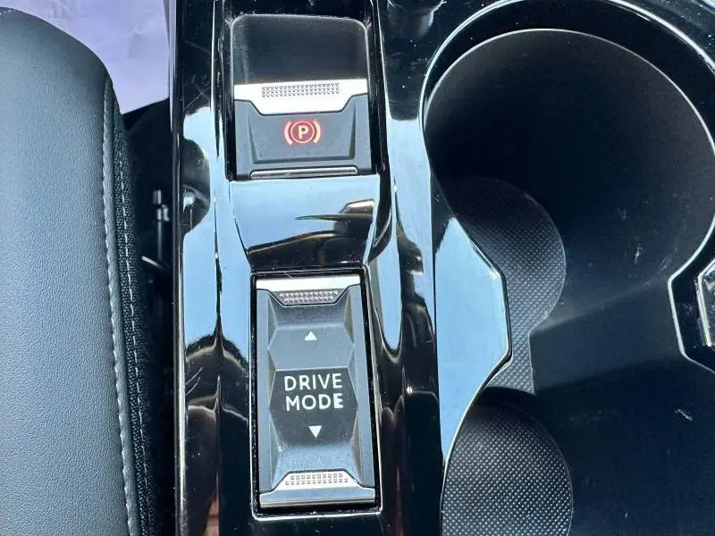 Gros plan sur la console centrale noire brillante du Peugeot 2008 avec bouton Drive Mode et frein à main électrique.