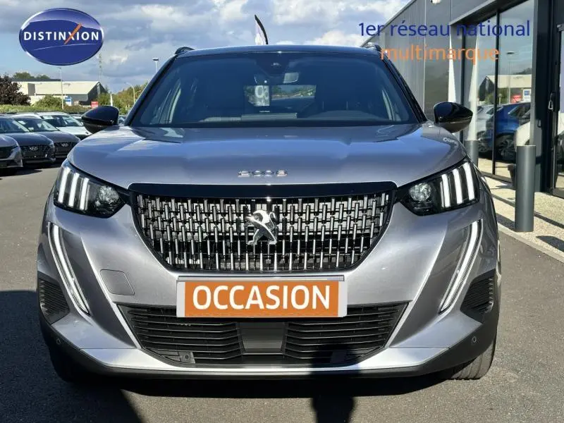 Vue frontale d'un Peugeot 2008 gris Artense avec calandre noire et feux LED verticaux, plaque "OCCASION" visible.
