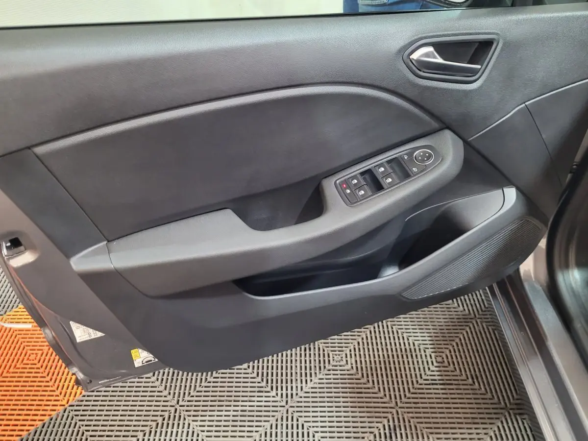 Vue intérieure côté gauche de la porte avant d'une Renault Clio gris foncé, avec commandes électriques des vitres et poignée intégrée.