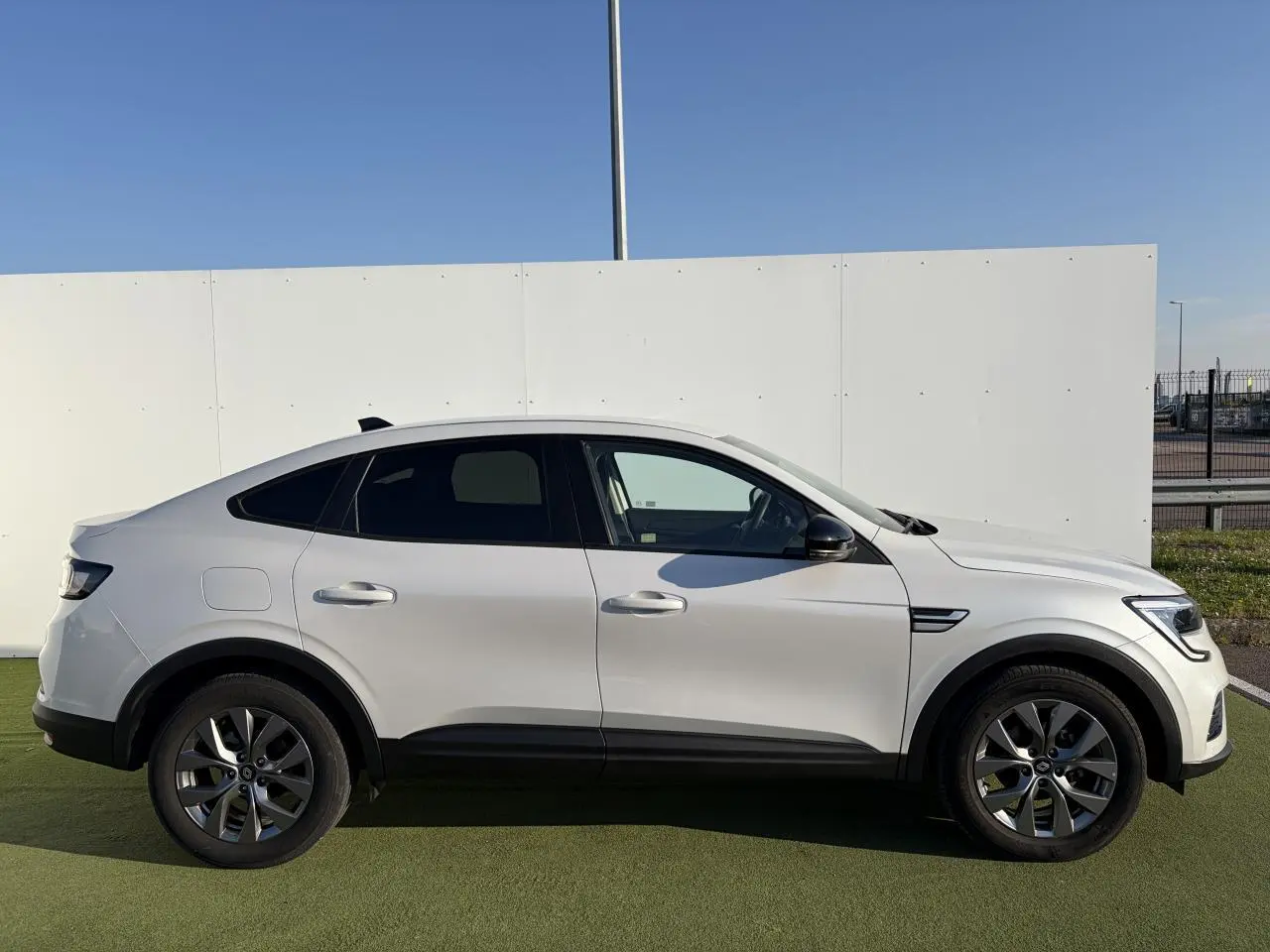 Profil droit d’un Renault Arkana blanc glacier 2025 avec jantes alliage grises et vitres surteintées.