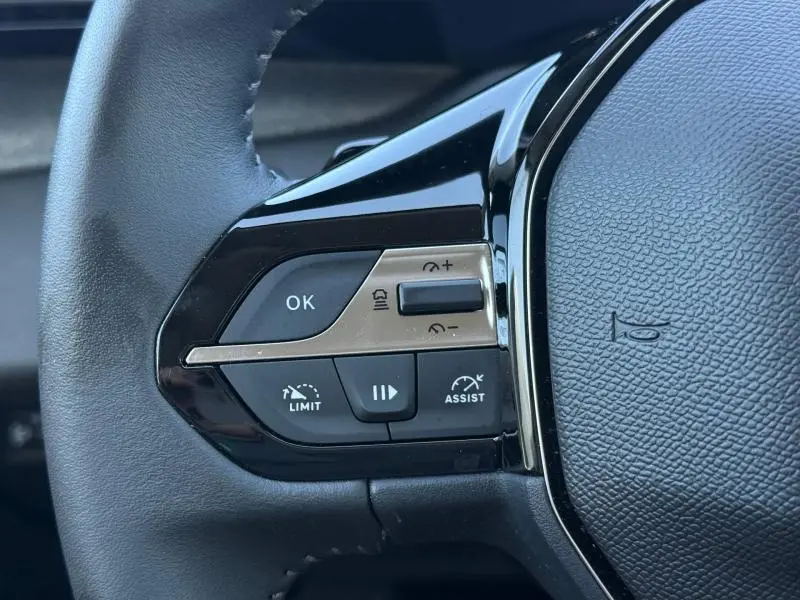 Gros plan sur les commandes gauche du volant noir du Peugeot 308 gris 2025, avec boutons de régulateur et assistance.
