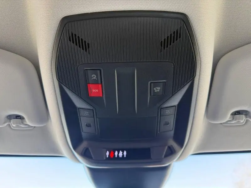 Vue en contre-plongée du panneau de commande de toit noir avec bouton SOS rouge dans un Peugeot 308 gris hybride 2025.