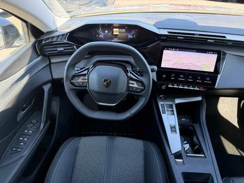 Vue intérieure frontale du poste de conduite gris de la Peugeot 308 Hybrid 2025 avec volant compact et écran tactile central.