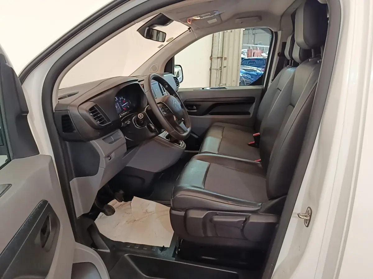 Vue intérieure côté conducteur du Citroën Jumpy blanc, montrant les sièges noirs et le tableau de bord moderne.