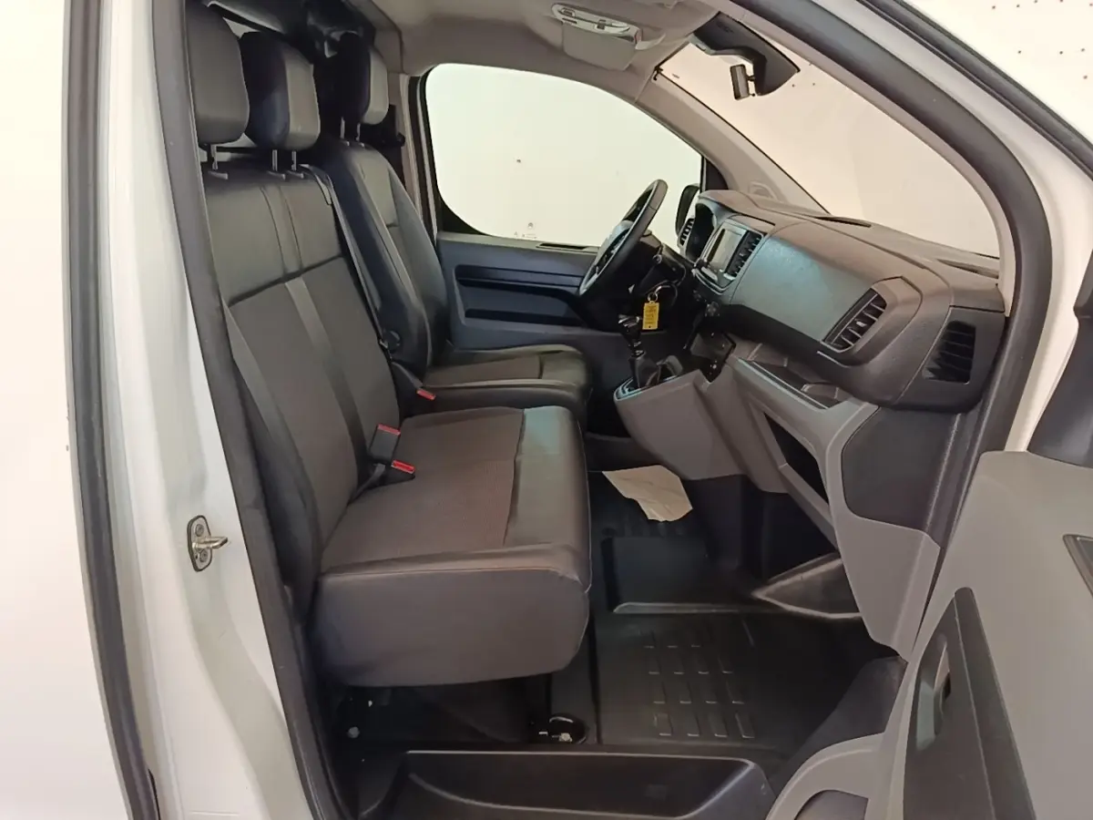 Vue intérieure côté conducteur du Citroën Jumpy blanc, montrant les sièges avant et le tableau de bord noir.