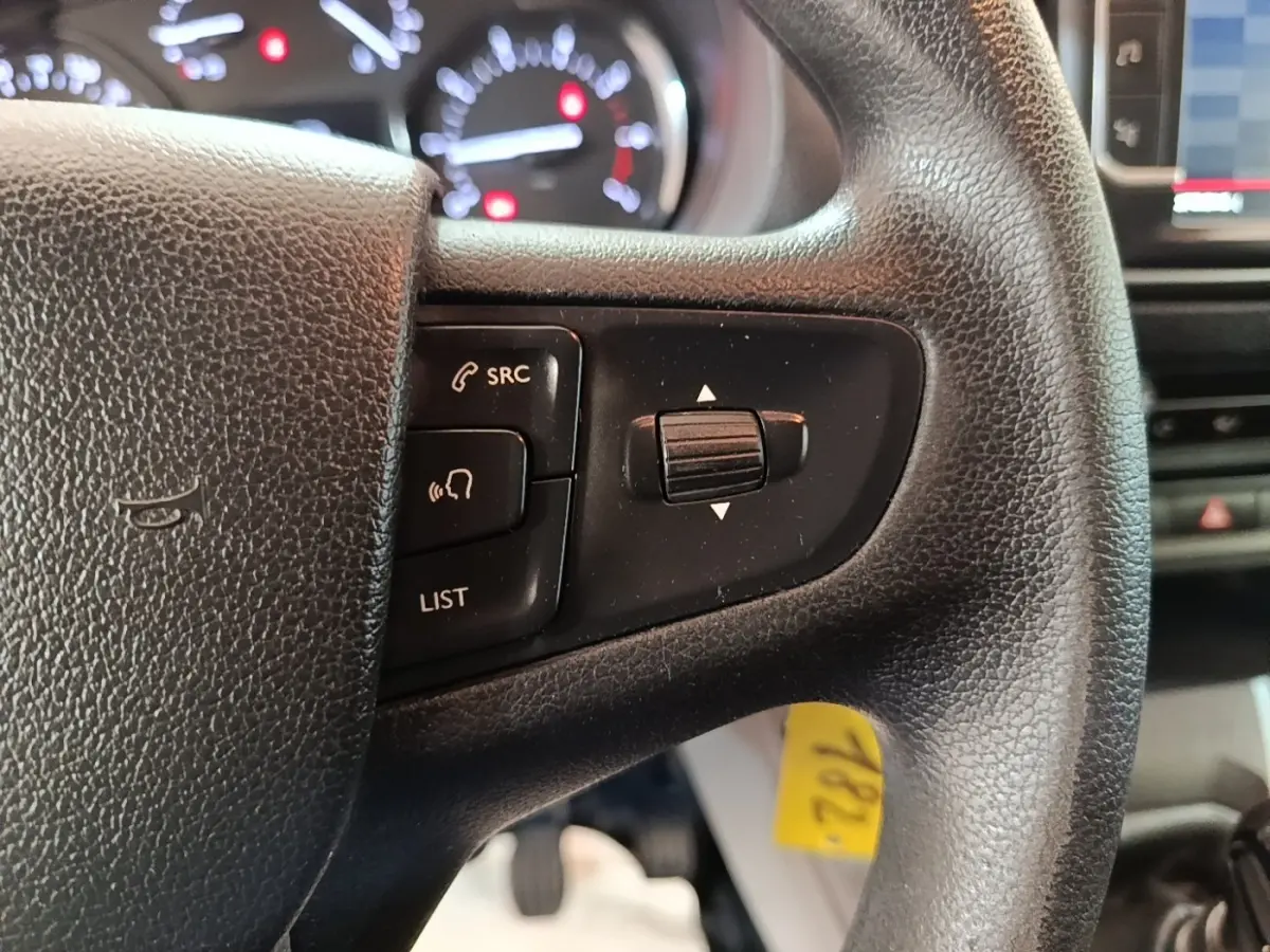 Gros plan sur le volant noir du Citroën Jumpy blanc, avec commandes audio et tableau de bord flou en arrière-plan.