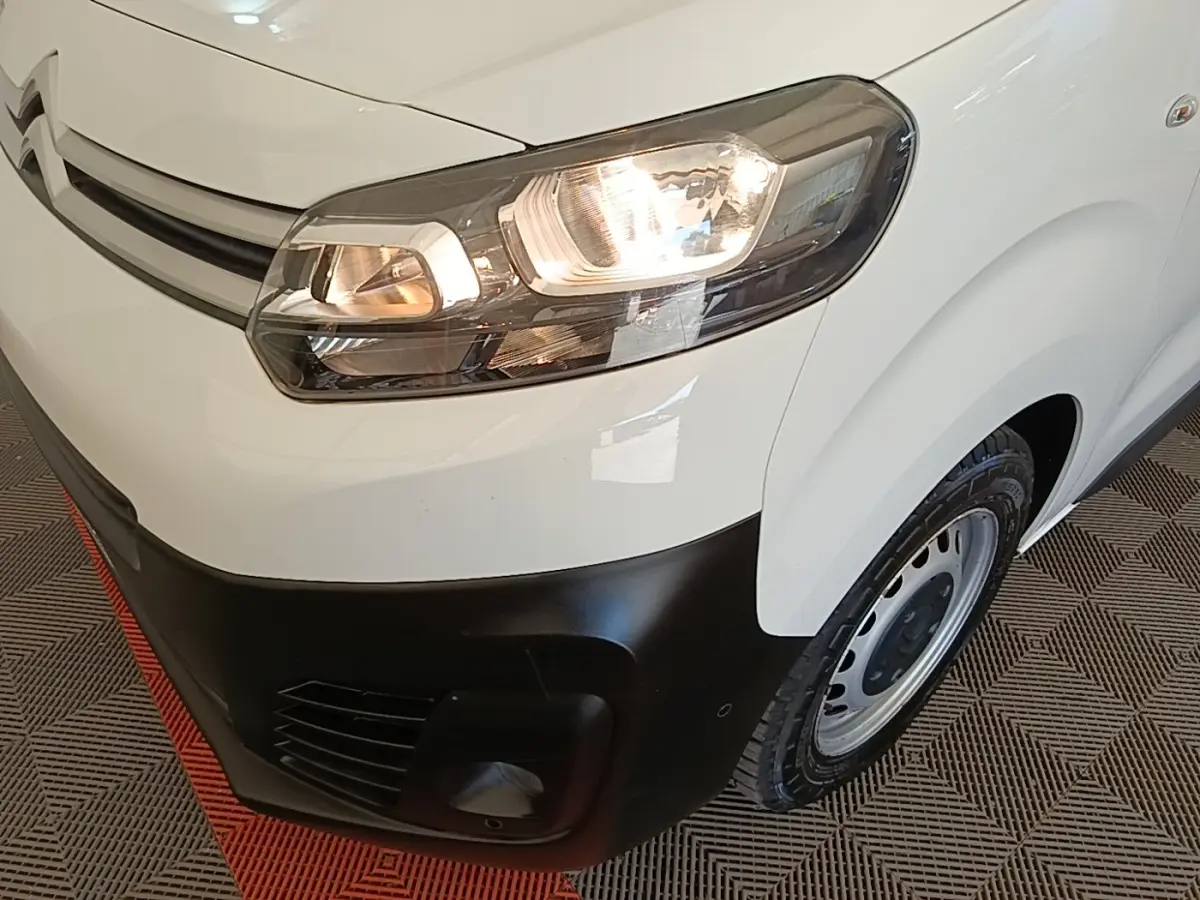 Vue rapprochée 3/4 avant droit du Citroën Jumpy blanc avec phares allumés et pare-chocs noir mat.
