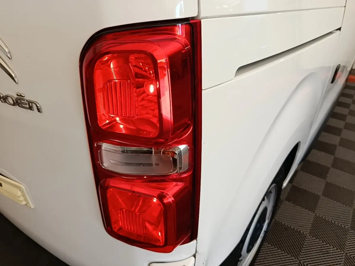 Gros plan sur le feu arrière gauche rouge d’un Citroën Jumpy blanc, avec partie latérale et roue visible.