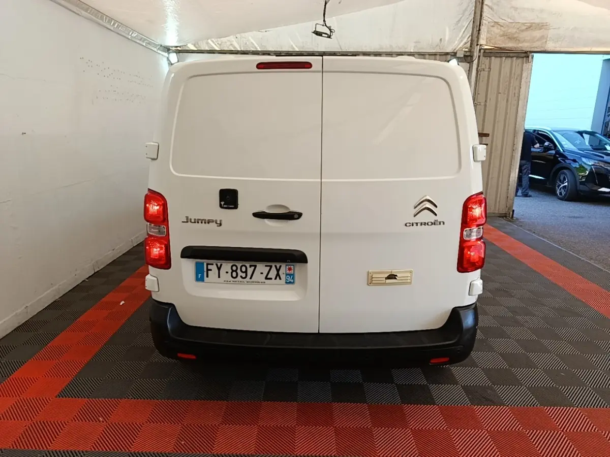 Vue arrière d’un utilitaire Citroën Jumpy blanc, portes battantes fermées avec plaques et feux rouges visibles.