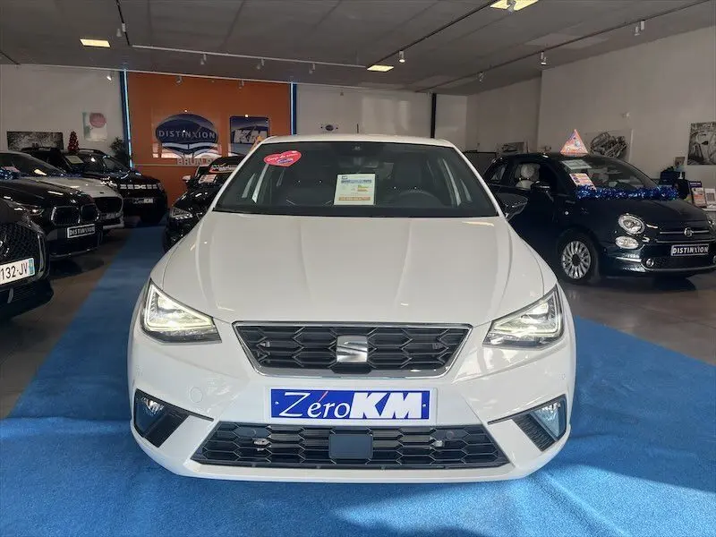 Vue frontale d'une SEAT Ibiza blanche Nevada Metal 2024 exposée en showroom avec plaque Zero KM visible.