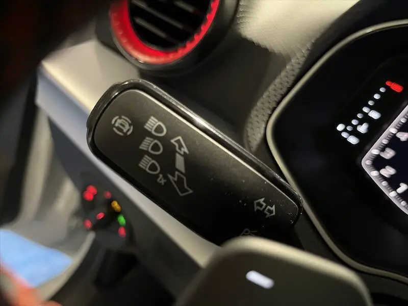 Gros plan sur la manette de clignotants et feux d'une SEAT Ibiza blanche Nevada Metal, intérieur avec aérateur rouge visible.