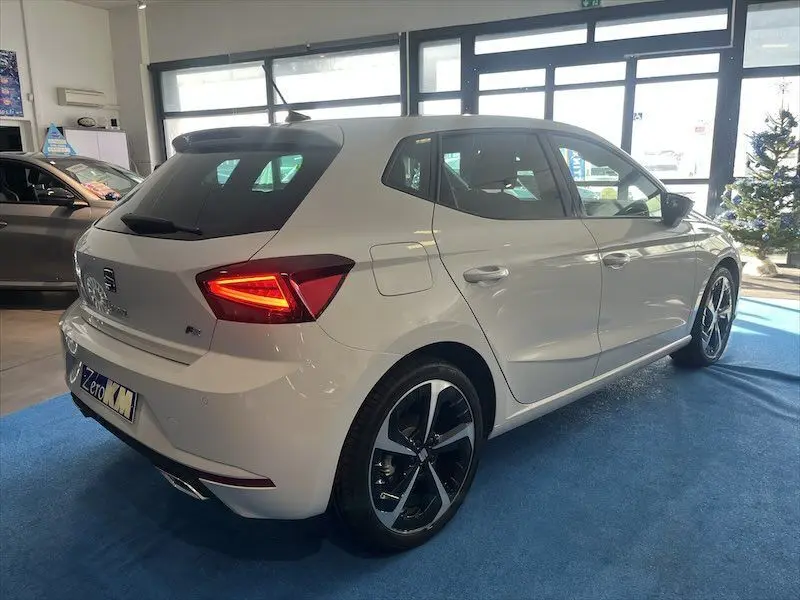 SEAT IBIZA 1.5 TSI blanc Nevada vue 3/4 arrière droit en showroom avec feux arrière allumés et jantes noires.