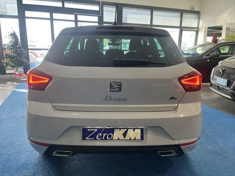 Vue arrière d'une SEAT Ibiza blanche Nevada Metal avec feux LED allumés et double sortie d'échappement chromée.
