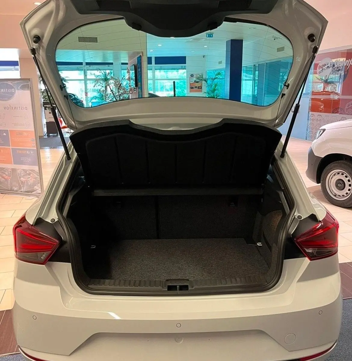 Vue arrière d'une SEAT Ibiza blanche Nevada Metal 2024 avec coffre ouvert et feux arrière LED visibles en showroom.