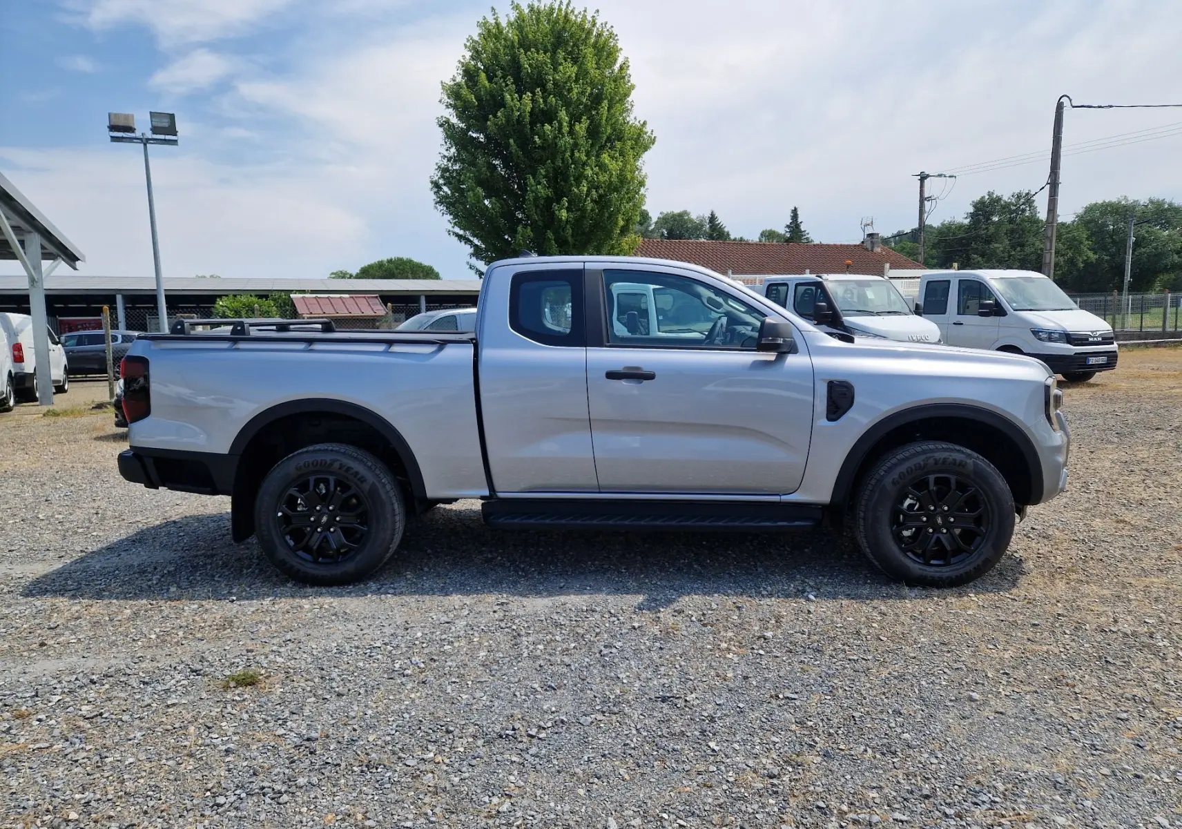 Vue latérale droite du Ford Ranger Super Cabine gris Iconic 2026 avec plateau équipé de barres et marchepied noir.